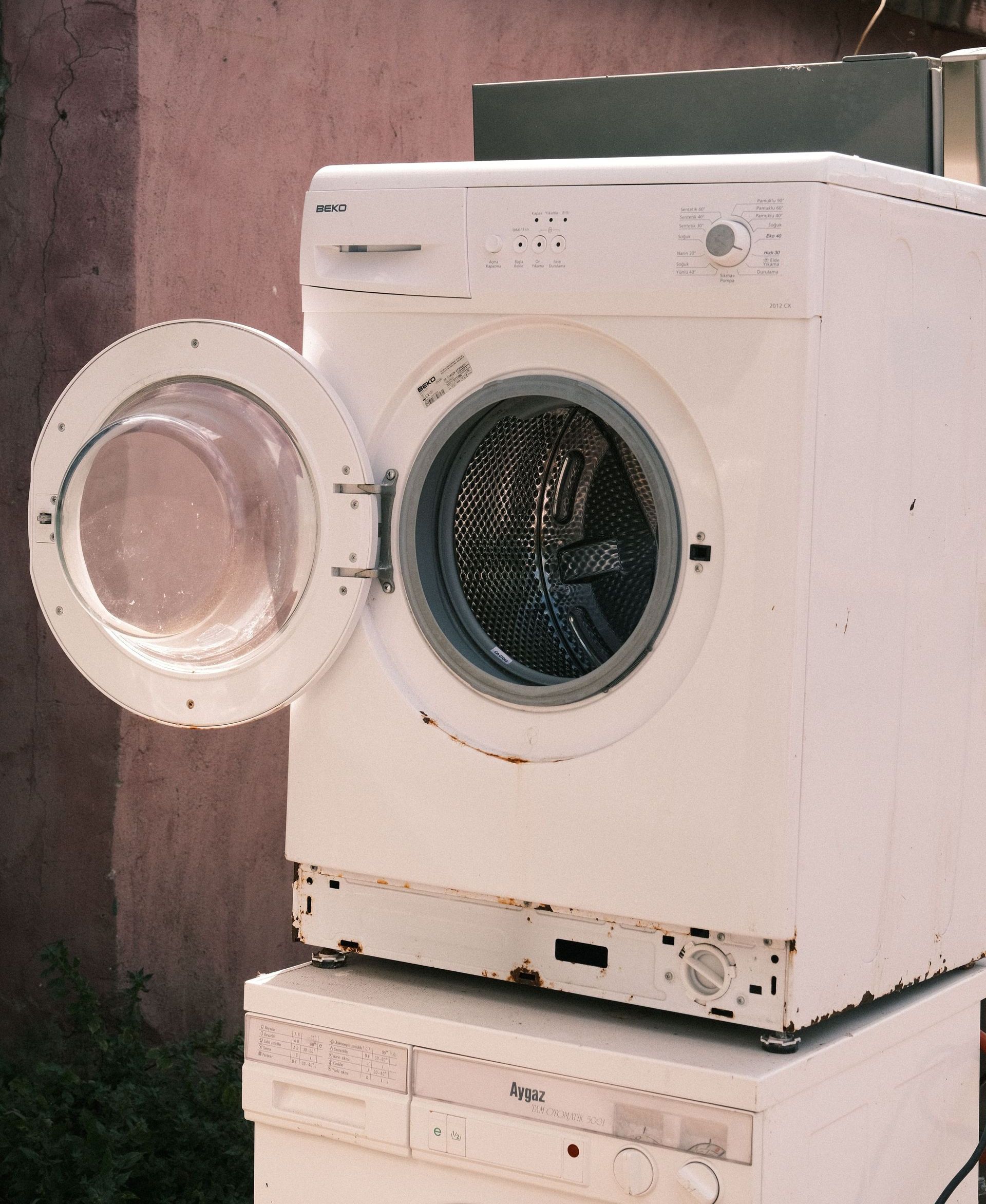 Outdoor view of two stacked laundry machines with an open door, showing rustic surroundings.