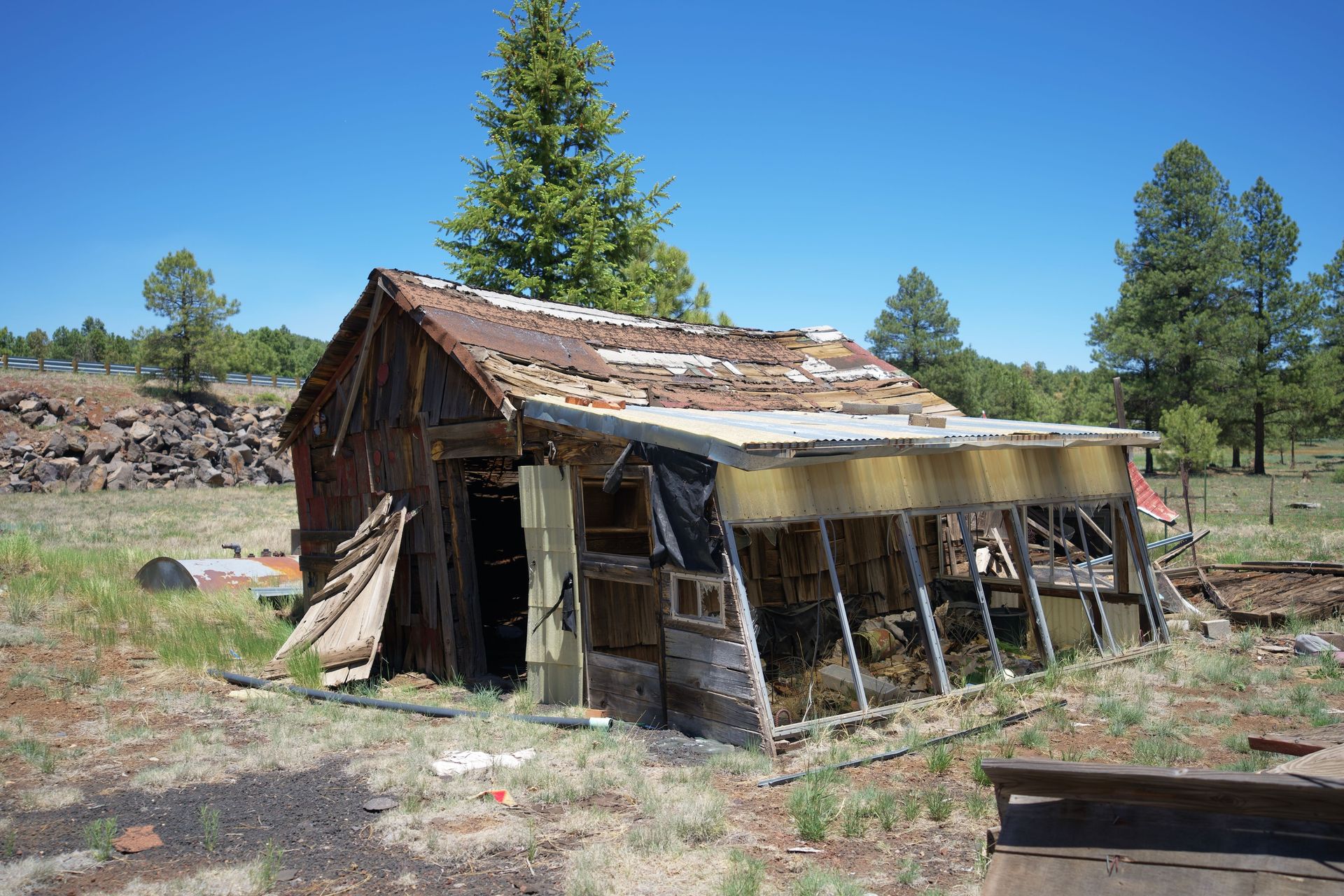 Rustic abandoned cabin in a grassy field under a clear blue sky.